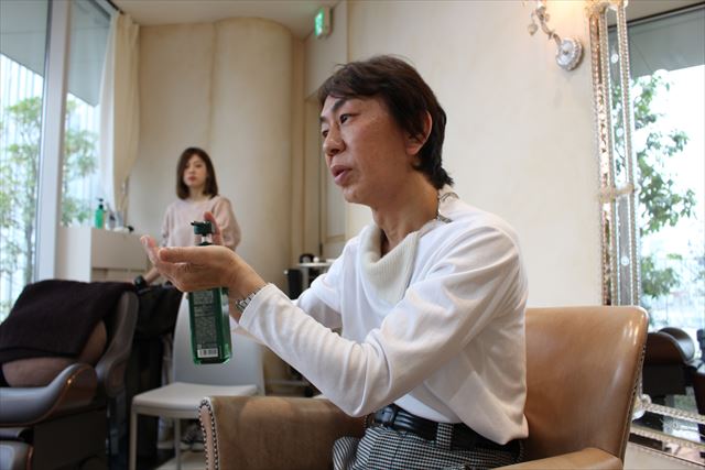 ZACCスカルプシャンプーのボトルを持ちながらテクスチャーについて説明する開発者の高橋和義さんの画像