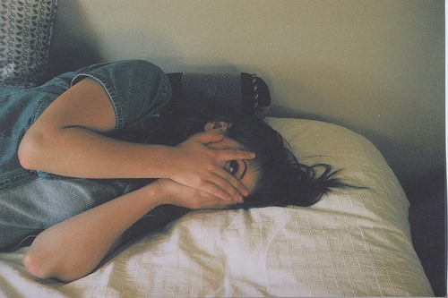 寝起きの顔を隠すベッドの女性